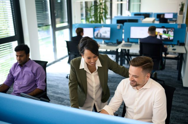 Eine Frau im Gespräch mit einem Kollegen im Großraumbüro