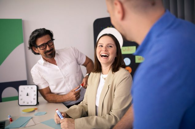Eine junge Frau lacht einen Kollegen an